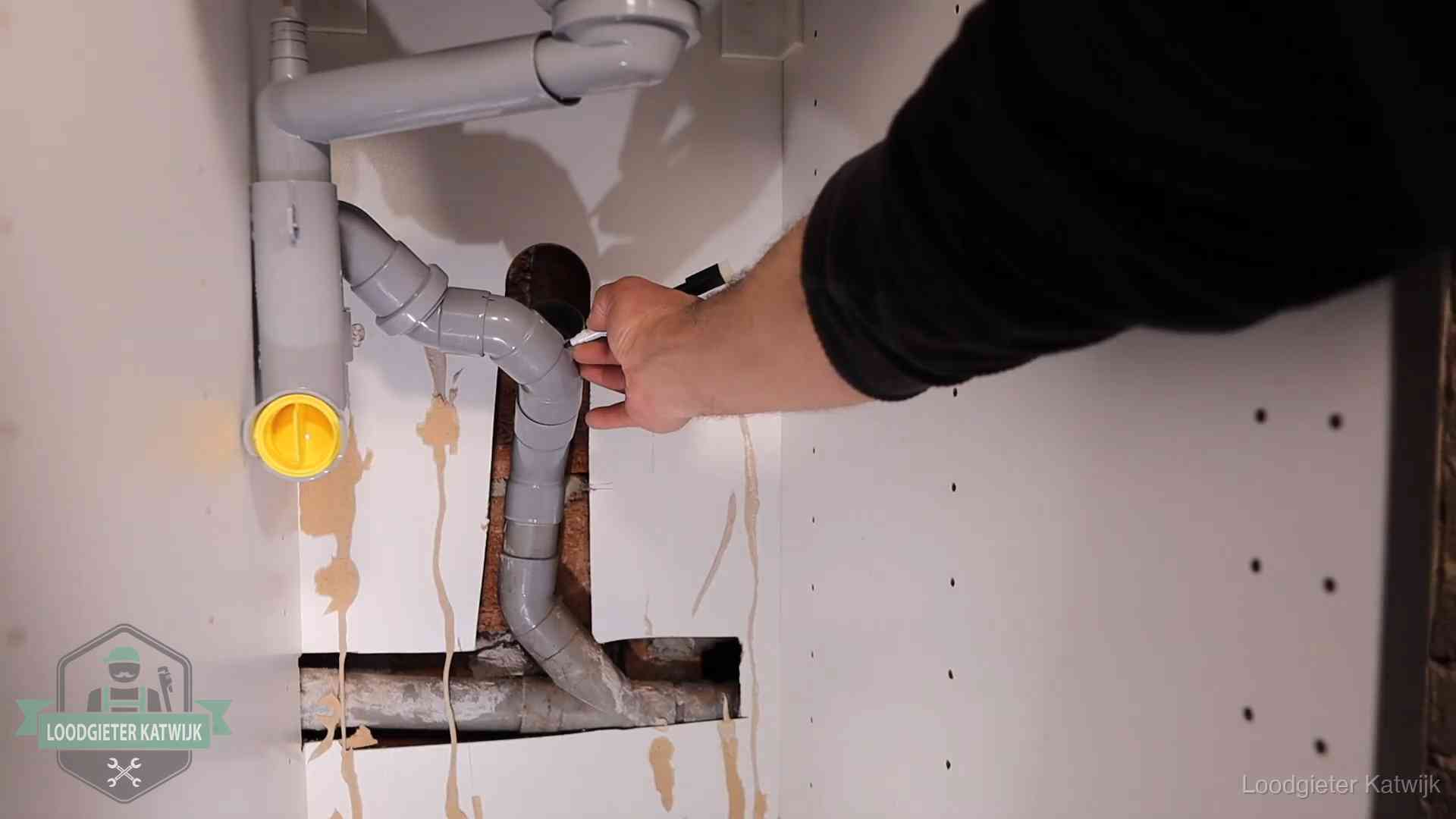 Loodgieter voor verhuurders en bedrijven in Katwijk Loodgieter markeert een pvc-afvoerbuis onder een gootsteen in Katwijk