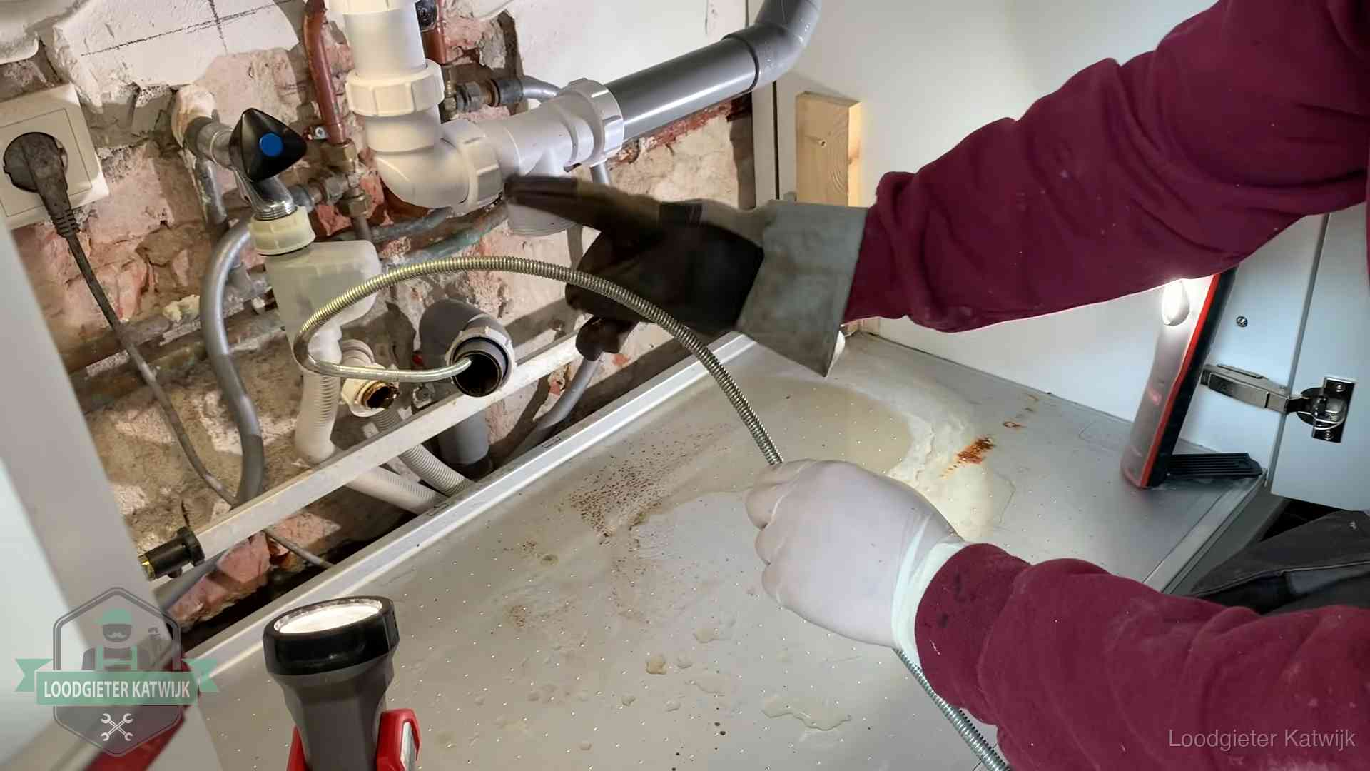 Ontstoppingsveer gaat in een geopende sifonaansluiting onder het aanrecht in Katwijk