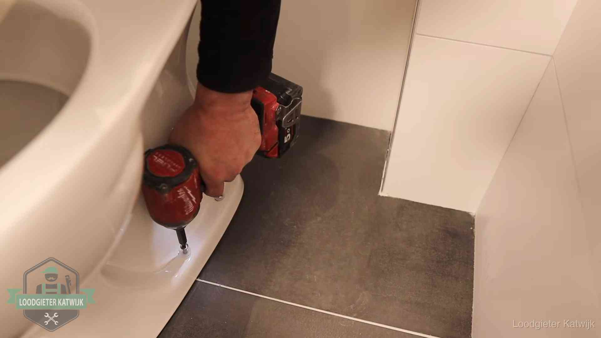 Kosten wc ontstoppen in Katwijk Loodgieter zet de voet van een wc-pot vast op de tegelvloer in Katwijk